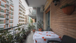 A balcony with a table covered in a tablecloth with floral patterns, potted plants, and a view of adjacent buildings. - Archidee by Ghor (Rome)