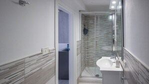 Et moderne badeværelse med et glasbadeværelsesafskærmning, en hvid vask og et spejl.
