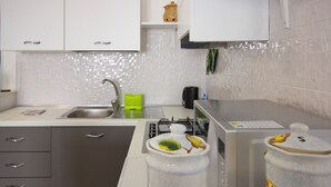 Uma cozinha moderna com armários brancos, uma pia de aço inoxidável e um fogão a gás. Há dois recipientes decorativos na bancada.