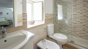 Um banheiro moderno com uma pia grande, bidê, vaso sanitário e chuveiro com divisória de vidro.