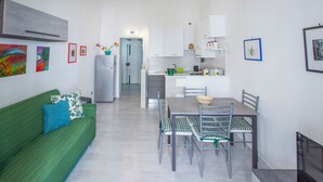 Uma cozinha moderna com armários brancos, uma mesa de jantar com cadeiras e um sofá verde com almofada azul.