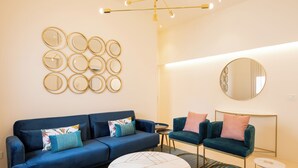 A modern living room with a blue sofa, two armchairs, a coffee table, and a wall-mounted mirror. - Amate Case by Ortigia Apartments (Syracuse)