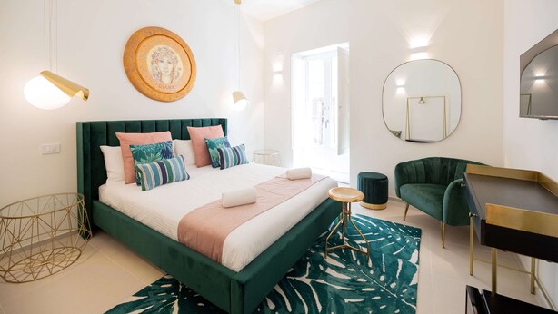 A modern bedroom with a green upholstered bed, a round mirror, and a desk with a chair. - Amate Case by Ortigia Apartments (Syracuse)