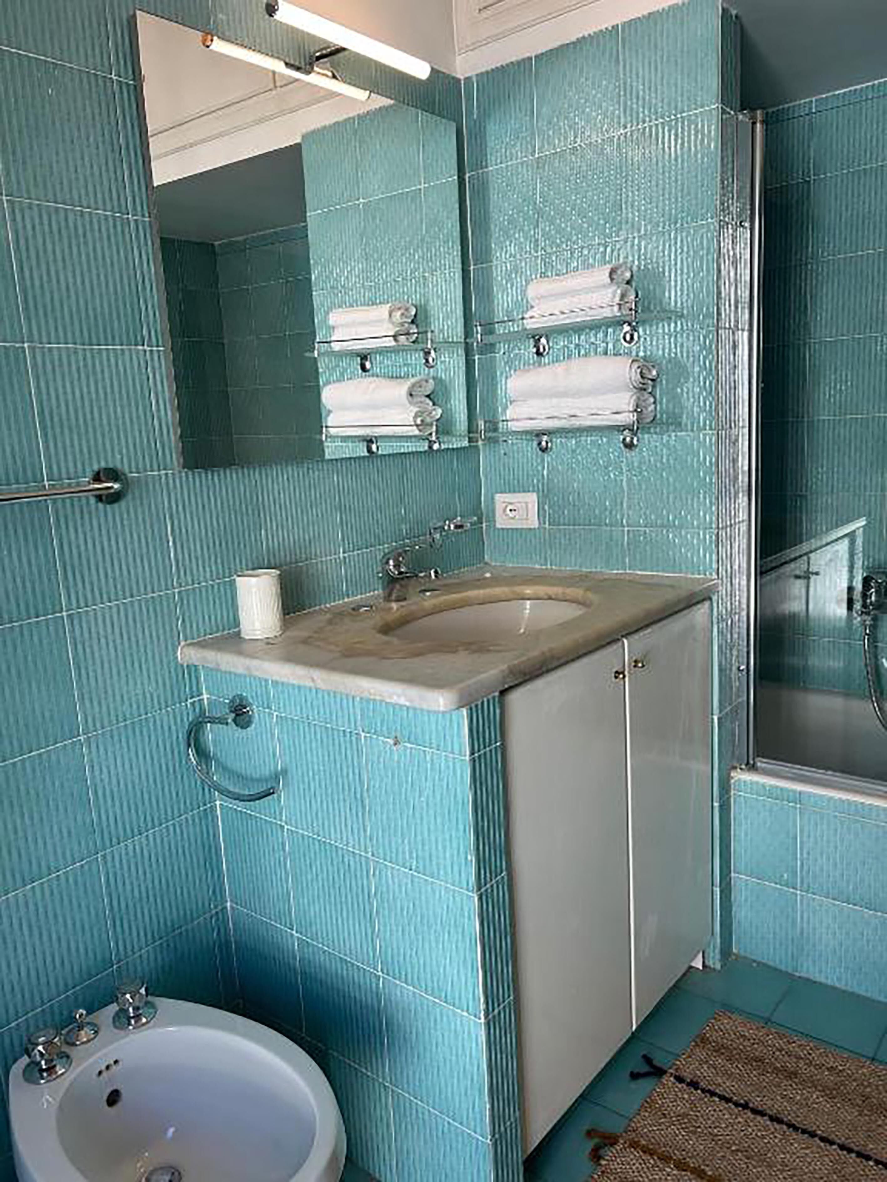 A bathroom with teal tiles, a sink, a mirror, and a shower.