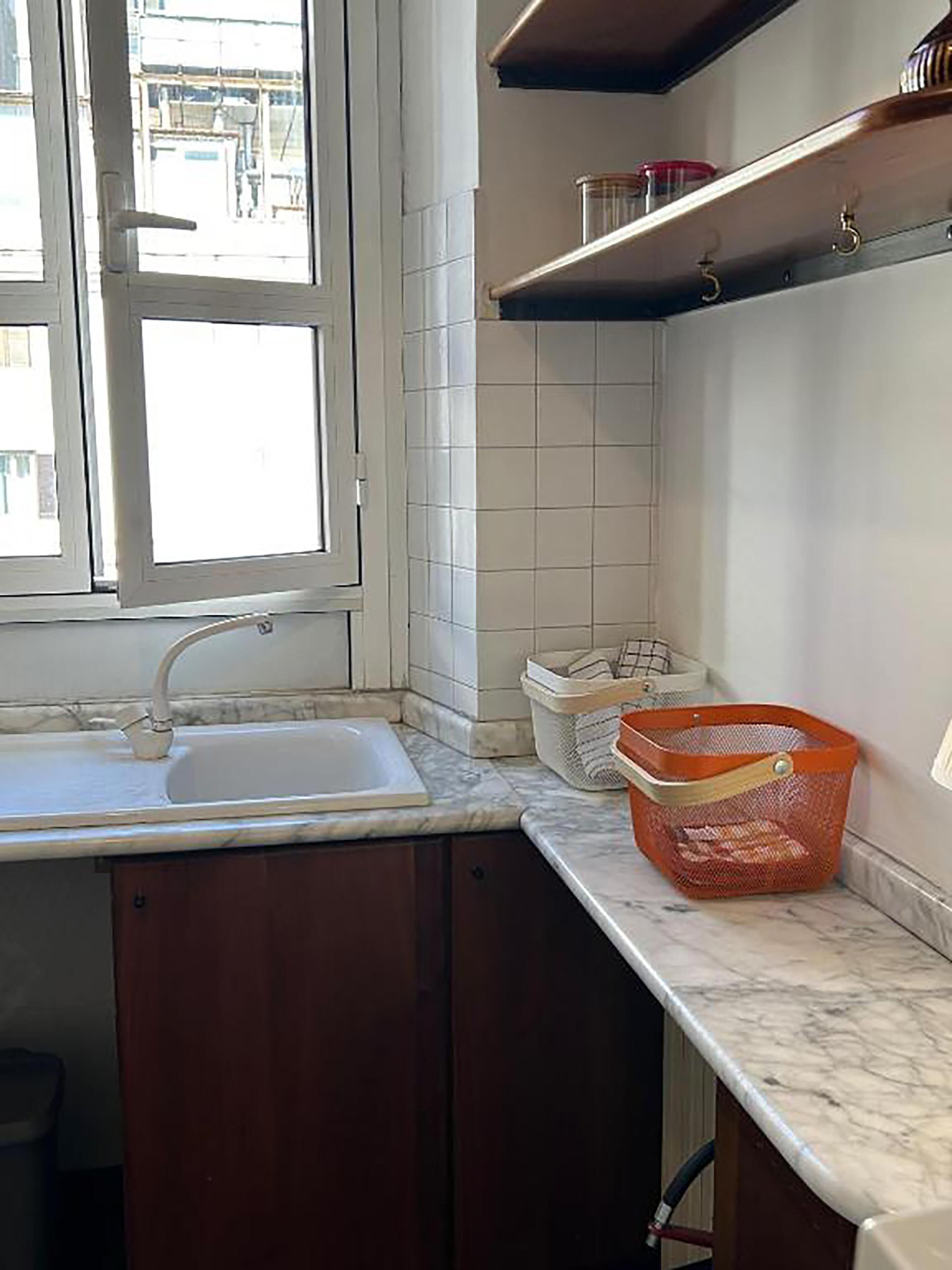 Una cocina con un lavamanos, armarios, una ventana y una encimera con una cesta.
