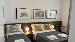 A hotel room with two beds, a nightstand with a lamp, and three framed pictures on the wall. - Termini Apartment by Ghor (Rome)