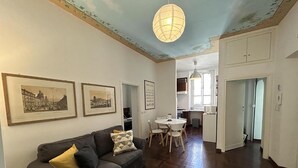 A living room with a dark grey sofa, a white dining table with four chairs, and a kitchen in the background. - Termini Apartment by Ghor (Rome)