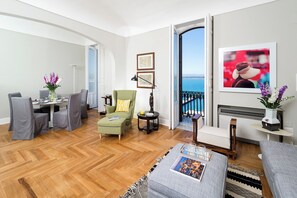 A modern living room with a dining area, a green armchair, a sofa, and a view of the sea through a balcony. - Duomo Sea View Suite by Ortigia Apartments (Syracuse)