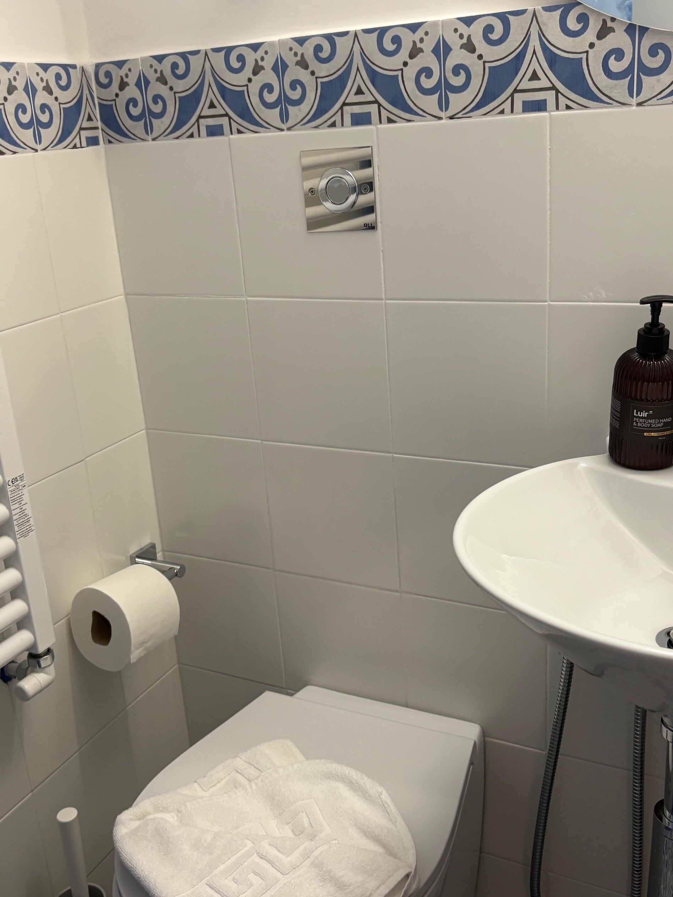A bathroom with a toilet, a roll of toilet paper, a towel, a sink, and a soap dispenser.