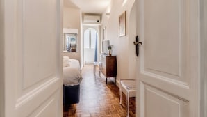 A hallway with a bed, a dresser, and a door with a cross. - Spagna Suite Dream by Ghor (Rome)