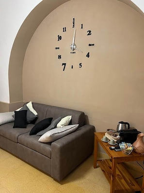 Un salon avec une grande horloge murale, un canapé et une table basse sur laquelle se trouvent une bouilloire et des tasses.