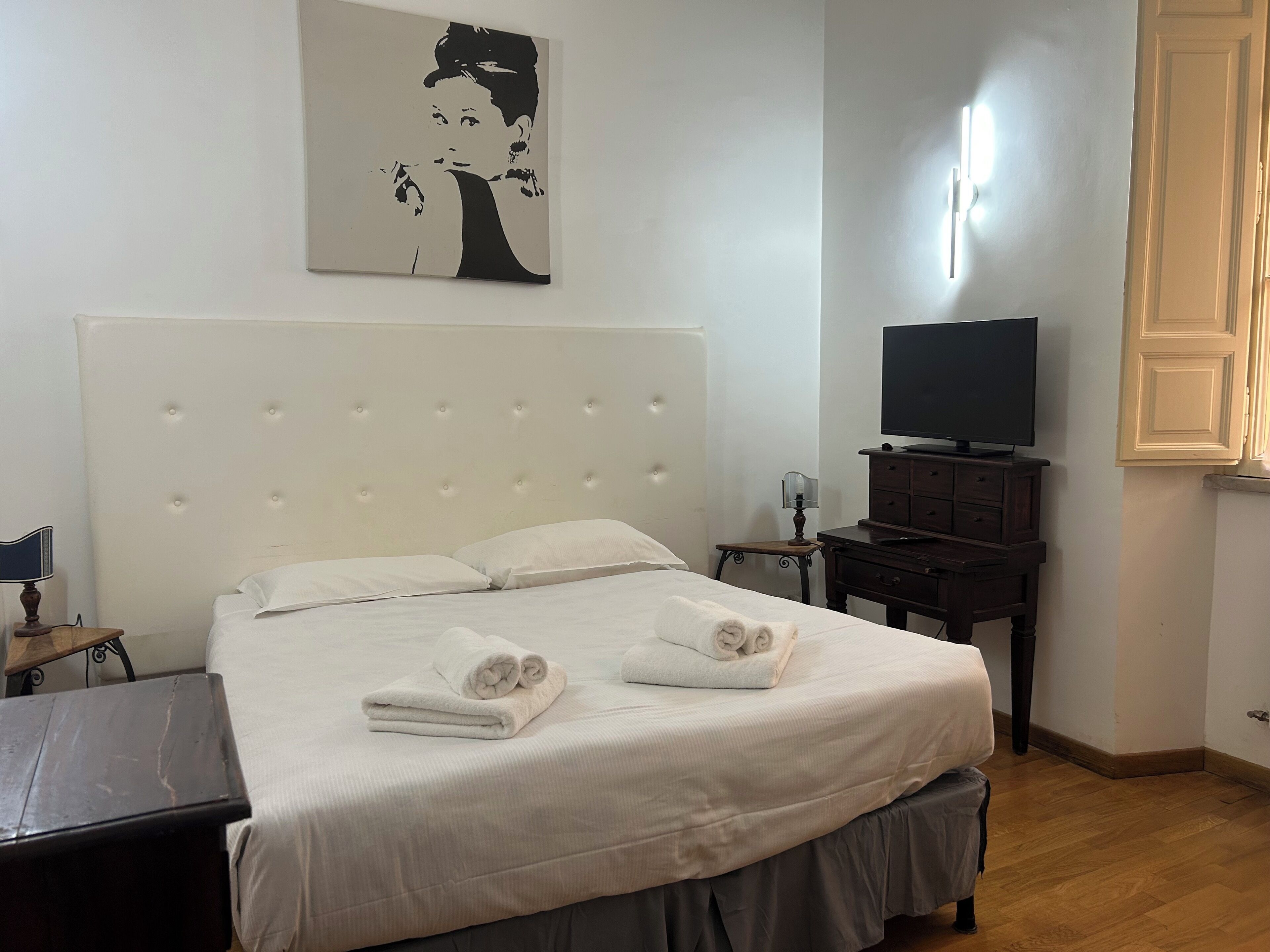 A neatly made bed with pillows and towels, a television on a dresser, and a painting on the wall.