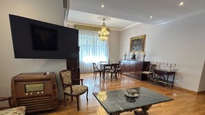 A living room with a flat-screen TV, a vintage radio, a dining table with chairs, a chandelier, and a painting on the wall. - Tiziano House by Ghor (Rome)