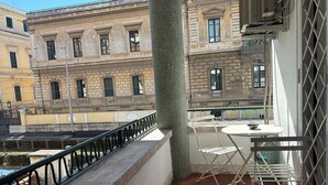 A balcony with a metal railing, a small table with a bowl, and a folding chair. - Tiziano House by Ghor (Rome)