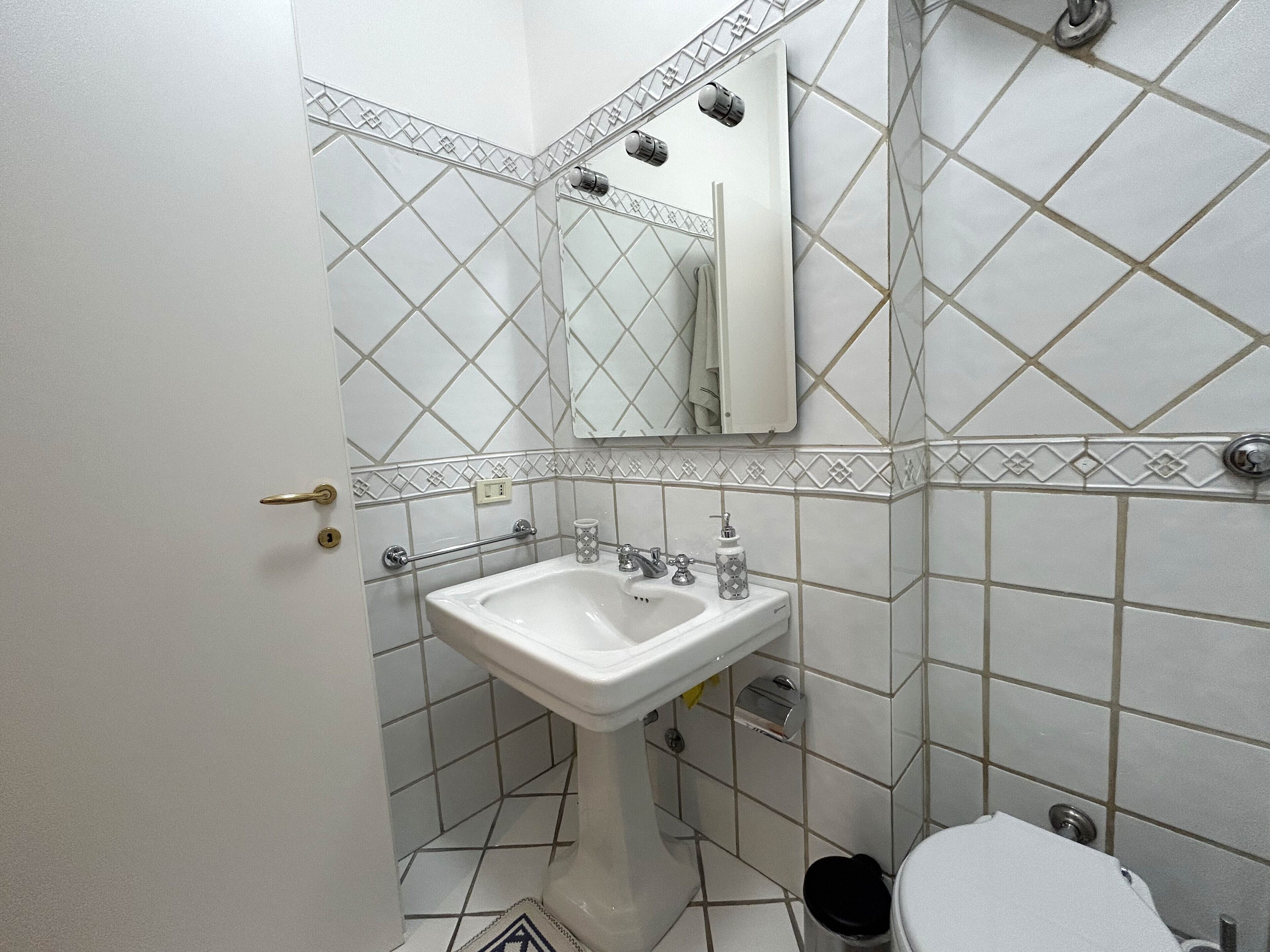 A bathroom with a white pedestal sink, a mirror, and a toilet.