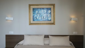 Quarto de hotel com uma cama grande, duas mesas de cabeceira, uma obra de arte emoldurada sobre a cama e luminárias fixadas na parede.