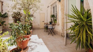 Un patio con plantas en macetas, una mesa con sillas y una puerta.