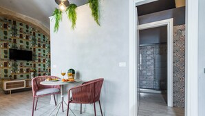 Un comedor con una mesa redonda, dos sillas de mimbre, un banco y un televisor instalado en la pared.