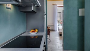 Une cuisine moderne dotée d’une cuisinière intégrée, d’un saladier rempli de fruits et donnant sur un espace de vie avec un canapé et des rideaux.
