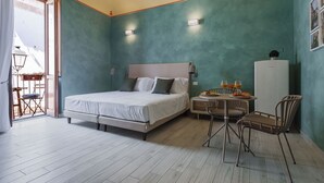 Un dormitorio con una cama, una mesa con sillas, un refrigerador y una ventana con cortinas.