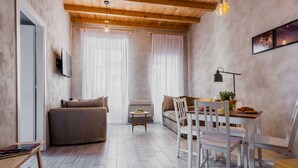 Een knusse woonkamer met een bank, een eettafel met stoelen, een salontafel en een aan de muur bevestigde televisie.