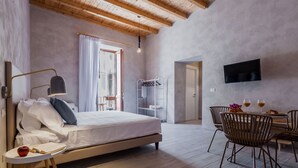 Een slaapkamer met een bed, nachtkastje, lamp en een zithoek met stoelen en een tafel.
