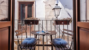 Een balkon met twee houten stoelen, een tafel en een hangplanter met bloemen.