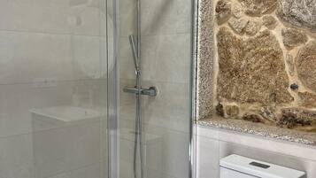 A modern bathroom with a glass-enclosed shower, a white toilet, and a stone wall.
