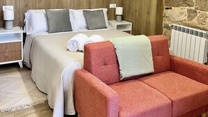 A bedroom with a stone wall, a bed with white bedding, a red sofa, and a white radiator. - Rural house Reibón (Moaña)