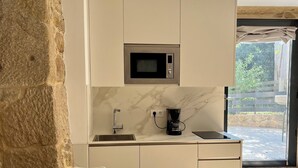 A compact kitchen with a built-in microwave, a sink, and a coffee maker. There is a dining table with chairs and a stone wall on one side. - Rural house Reibón (Moaña)