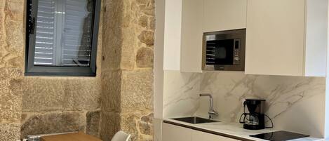 A compact kitchen with a stone accent wall, a dining table with chairs, a built-in microwave, and a coffee maker.