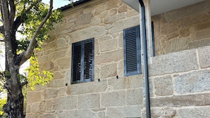 A stone building with two windows and a door, surrounded by a tree and a flower bed. - Rural house Reibón (Moaña)