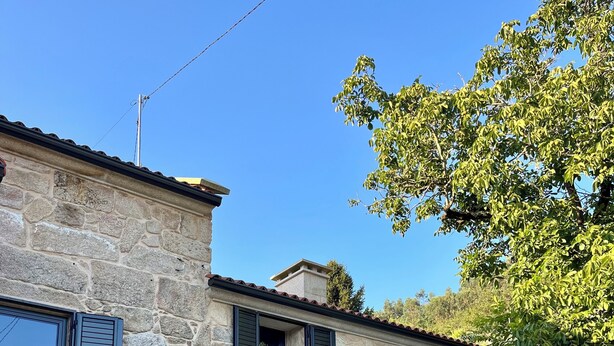 A stone building with a staircase leading to a door, a table with chairs, and a tree in the background. - Rural house Reibón (Moaña)