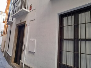 Un vicolo stretto con edifici su entrambi i lati. Una parete bianca con una finestra a destra e un portone a sinistra.