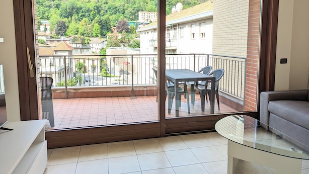 A balcony with a glass door, a table with chairs, and a sofa. - Spina Verde (Como)
