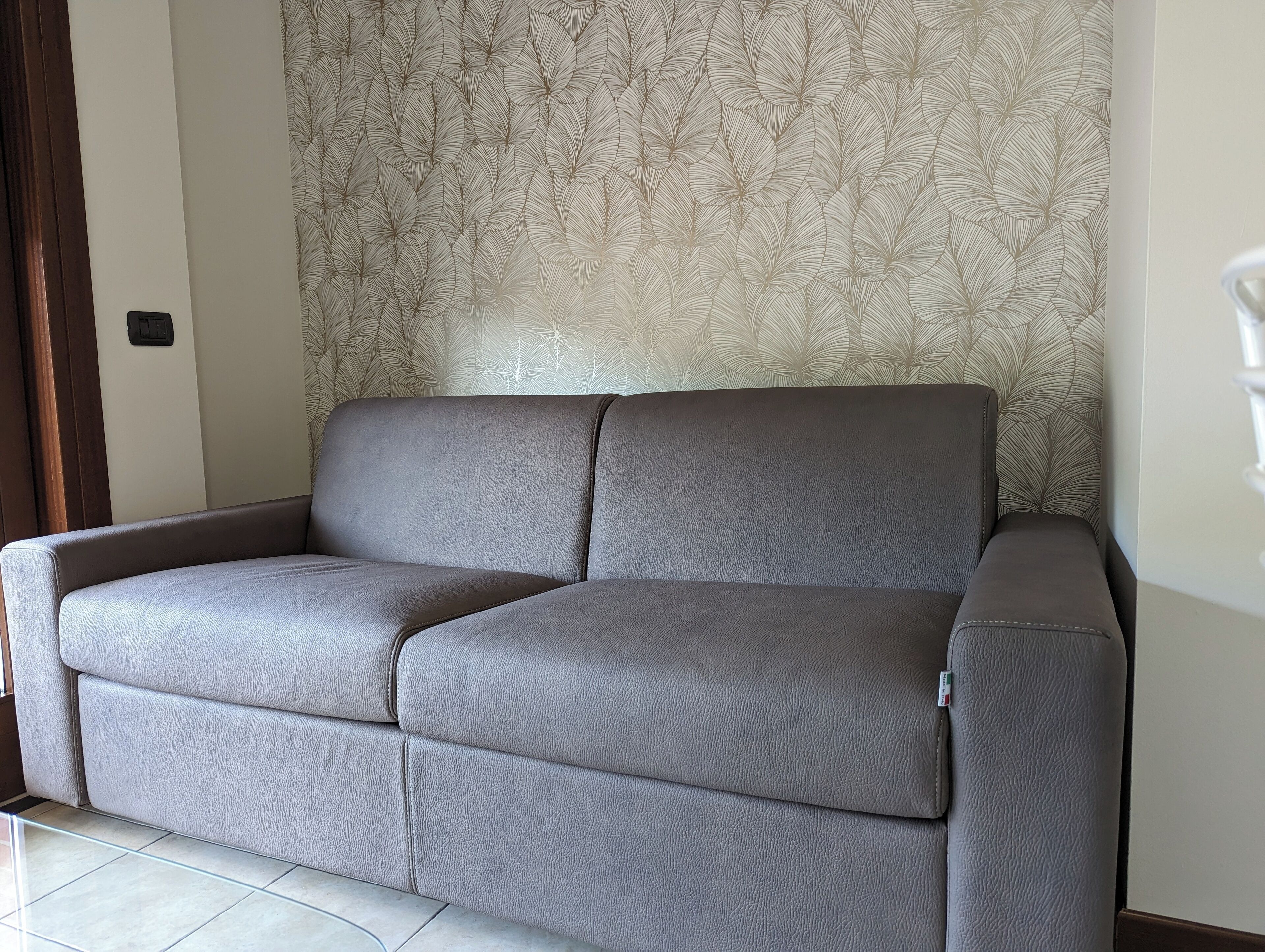 Un sofá gris con tela texturizada, frente a una pared con papel tapiz estampado con hojas.