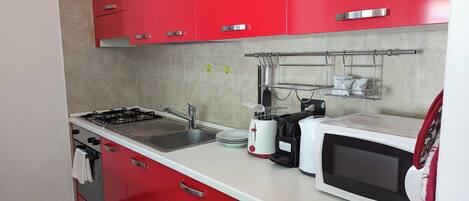 A modern kitchen with red cabinets, a gas stove, a sink, a toaster, and a microwave.