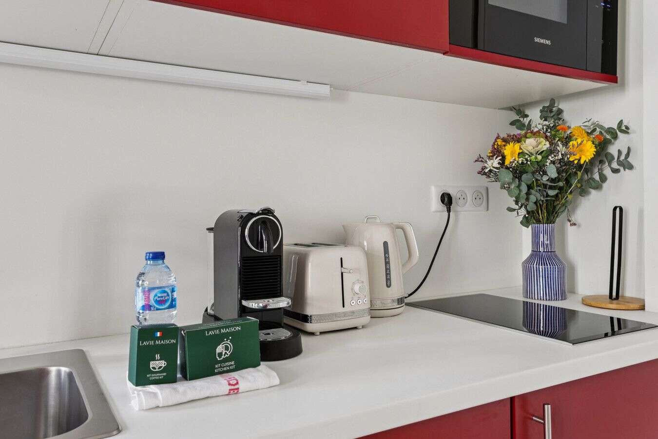 A kitchen counter with a water bottle, coffee maker, toaster, kettle, and a coffee kit.