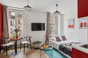 Kompakti hotellihuone, jossa on sänky, pieni ruokailutila pöydällä ja tuoleilla, seinälle asennettu televisio ja näkymä kaupunkiin suurista ikkunoista.
