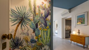 A hallway with a cactus mural, a wooden dresser, and a kitchen in the background. - Casa Lumia by Ortigia Apartments (Syracuse)
