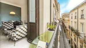A balcony with a view of a narrow street, a chair, a table, and a potted plant. - Casa Lumia by Ortigia Apartments (Syracuse)