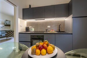 Eine moderne Küche mit grauen Schränken, einer Edelstahl-Spüle und einem Glastisch mit Obstschale.