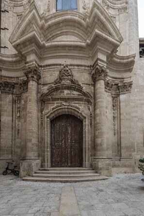 A stone building with a large wooden door, steps leading up to it, and a small bicycle parked nearby. - Casa Lumia by Ortigia Apartments (Syracuse)