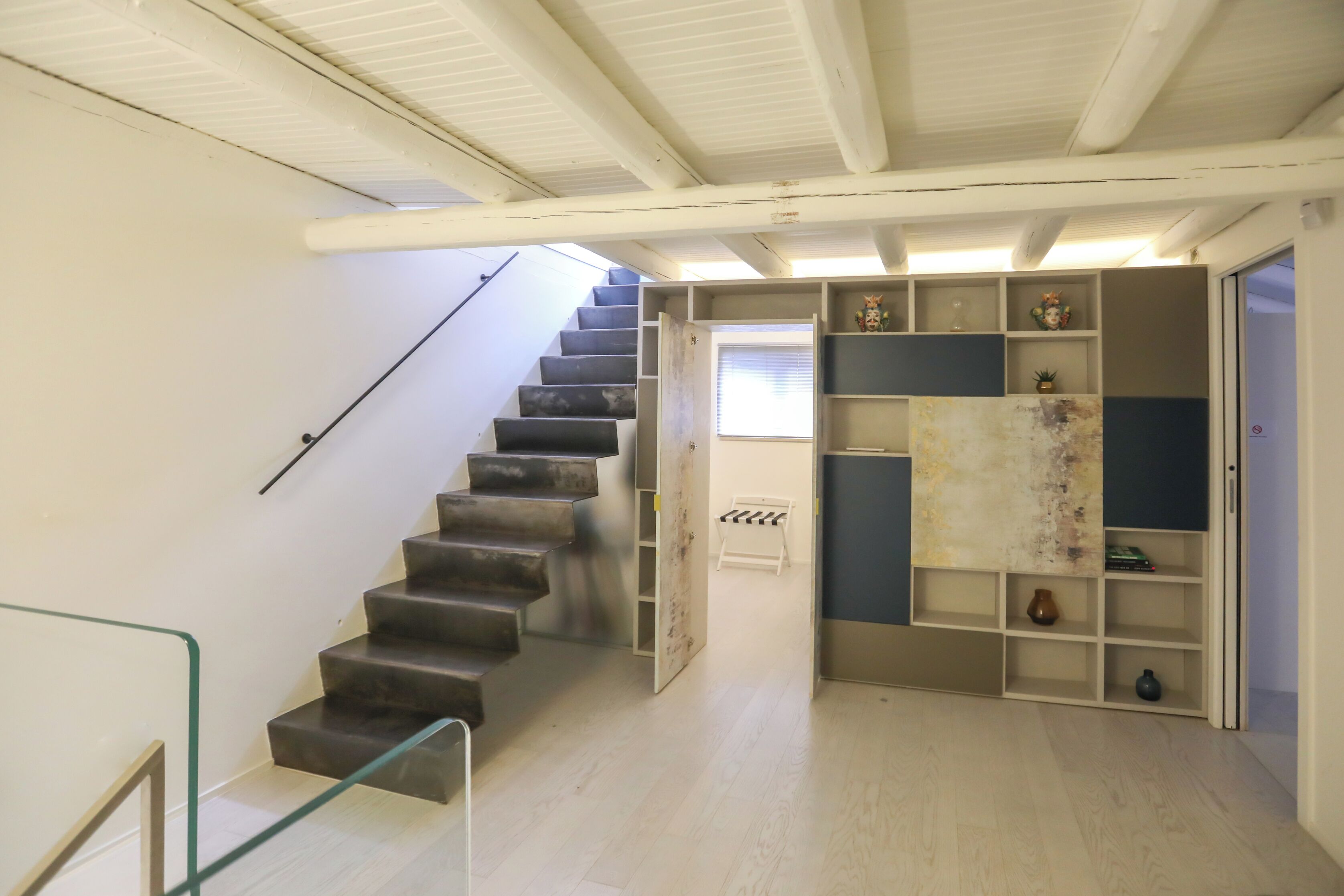 A staircase leading to a landing with a glass railing, a wooden floor, and a built-in shelving unit with decorative items.