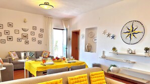 A dining area with a yellow tablecloth, a sofa with yellow cushions, and a wall with various decorations including a compass and framed butterflies.