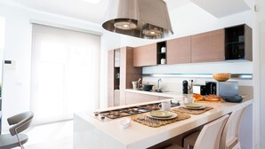 A modern kitchen with a central island, stainless steel appliances, and a pendant light. - Villa Elena by Ortigia Apartments (Isola)