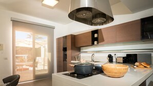 A modern kitchen with a central island, stainless steel appliances, and a sliding glass door leading to an outdoor area. - Villa Elena by Ortigia Apartments (Isola)