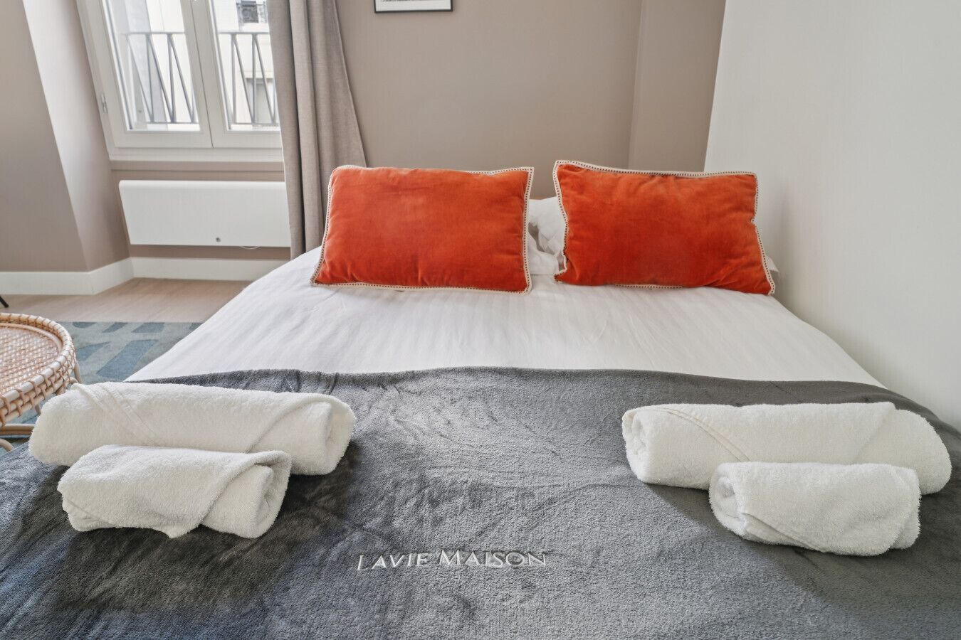 A hotel room with a bed, two orange pillows, a gray blanket, and two white towels.