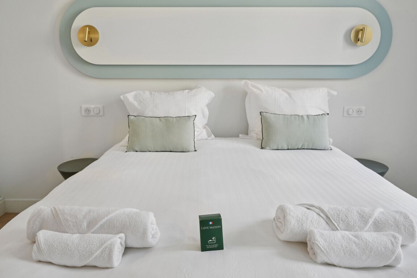 Una cama bien hecha con sábanas blancas, dos almohadas y dos toallas enrolladas.