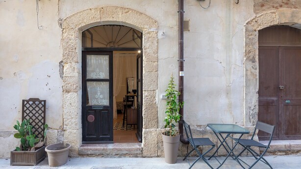 Un edificio con un portale ad arco, una pianta in vaso e posti a sedere all'aperto.